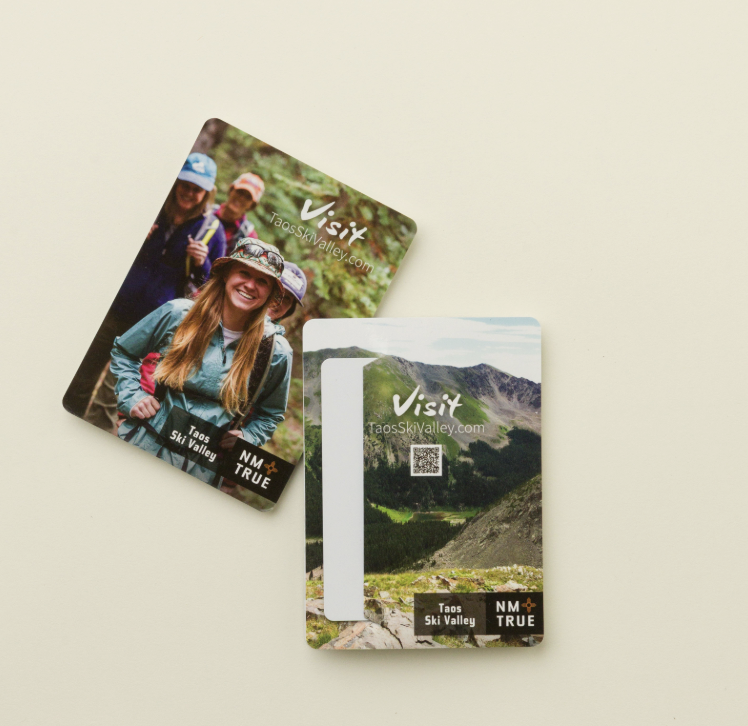 Two Visit Taos Ski Valley pocket maps, one featuring smiling hikers and the other designed with a room key slit and scenic mountain imagery, ideal for hotel and travel use.